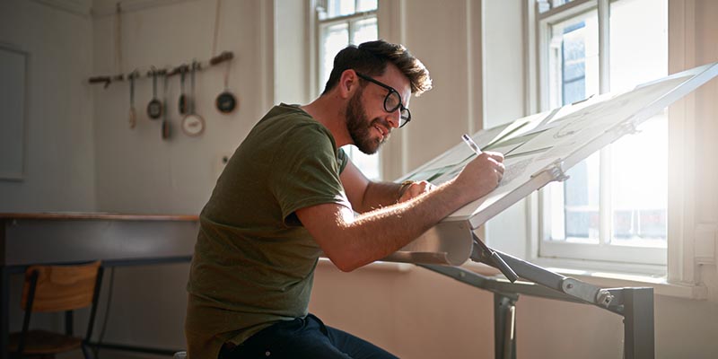 A man sits at a design desk drawing something